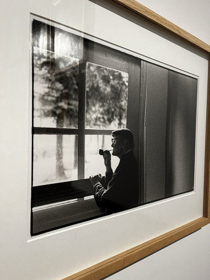 Un homme à la pipe et casquette regarde par la fenêtre 