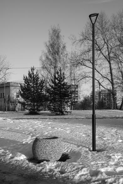 The monochrome photo shows a laconic winter composition of a lantern and a granite flower bed.