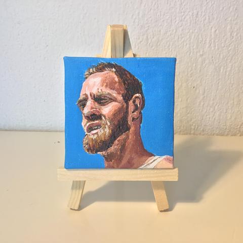 Small 3 quarter portrait of a man with a brown beard in the bright sunshine, against a sky blue background