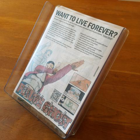 Transparent acrylic document tray holding 200 copies of the flyer for WIP indie game 'Future Ghost', partially elevated at an angle from the timber tabletop on which it stands.