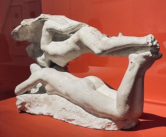 Sculpture by Auguste Rodin (1840-1917) called Le Rêve ou le Baiser de l'ange, against a red background.
Rediscovered in the 1980s, this work combines the female figure of Sorrow, taken from the Gates of Hell, with the angel from The Fall of Icarus. This highly sensual group shows a levitating angel brushing past the body of a sleeping woman: "This is dream, said Rodin, he is visiting this woman while holding his wings with one hand, so as not to make any noise" (Judith Cladel). 
This composition is built around a void, removed from the marble kept in the collections of the Thyssen-Bronemisza Museum (Madrid). This plaster cast, with its reference points, was its original matrix. 