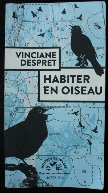 Couverture du livre de Vinciane Despret 'habiter en oiseau'. Y sont représentés deux oiseaux noirs  en avant-plan, très contrastsé, sur un fond bleu clair passé. Le fond est constitué d'une composition reprenant des éléments d'une carte topographique découpée en zones territoriales indiquées par des pointillés. Sur ce fond planent des oiseaux de plus petites tailles.