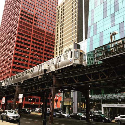 A subway train traveling southbound on the elevated tracks above Wabash Avenue. Behind it are three skyscrapers in red, yellow and blue. 