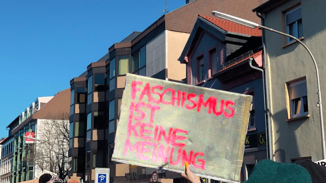 In der Demo hält bei strahlend blauem Himmel eine Person ein Schild hoch: FASCHISMUS IST KEINE MEINUNG!