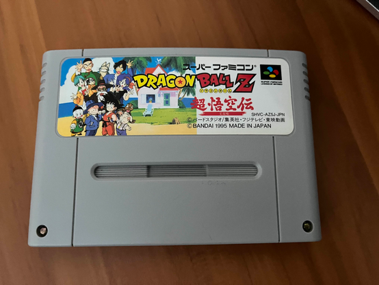 Super Famicon/SNES game cartridge for Dragon Ball Z: Super Gokuden: Totsugeki-Hen (Dragon Ball Z: Super Goku's Story: Assault Arc) sitting on a desk.