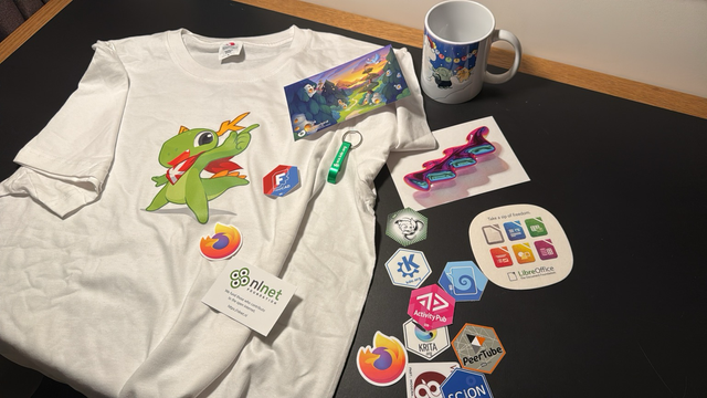 A bunch of stickers a mug and a tshirt. All have various open source project logos on them. 