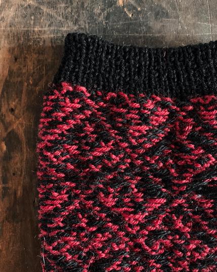 Detail of a Knitted sock turned inside out, showing the yarn floats from colorwork knitting. The pattern is is red and black with a black cuff