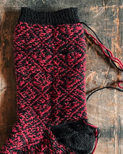 Detail of a Knitted sock turned inside out, showing the yarn floats from colorwork knitting. The pattern is is red and black with a black cuff and heel