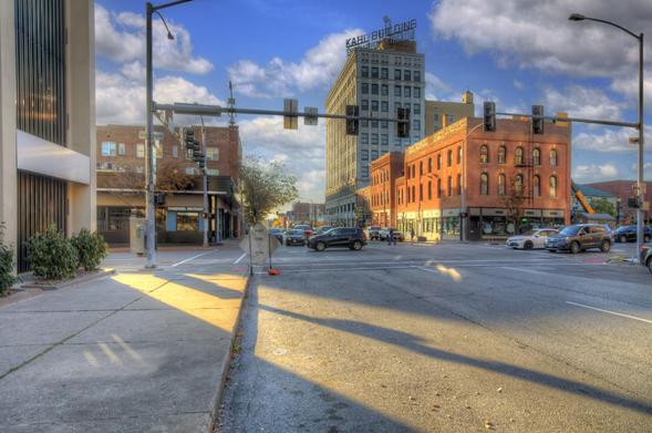 A busy intersection features several cars stopped at a traffic light, with sunlight casting long shadows across the street.