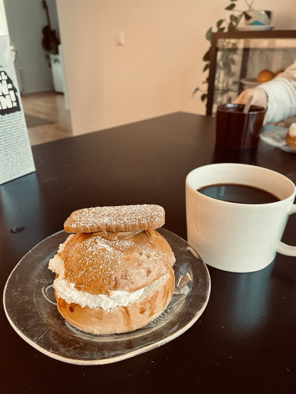 Kuvassa kahvikuppi, jossa mustaa kahvia ja biscoff-laskiaispulla. 