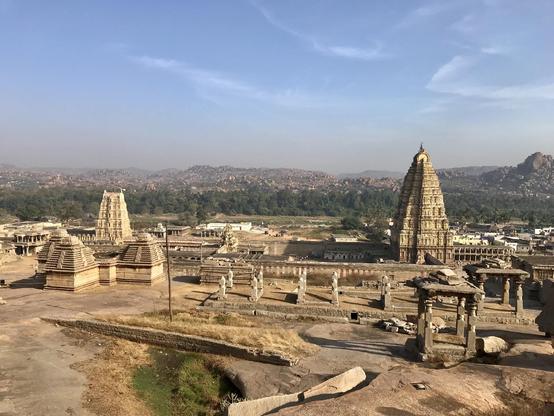 Das Foto zeigt die Aussicht vom Hemakuta Hill in Hampi auf den VirupakshaTemple aus dem 9. Jahrhundert. Besonders beeindruckend ist die rechts im Bild aufragende neunstufige Gopura/Torturm. Das Foto ist in etwa in der Höhe der Spitze dieser Gopura gemacht worden. Links im Bild ist noch eine fünfstufige, in der Mitte zum Tempeleingang eine dreistufige Gopura zu sehen.