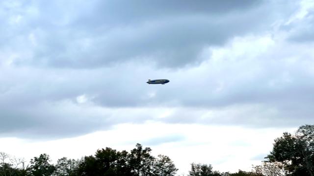 The Goodyear blimp floating in a cloudy sky with trees partially visible at the bottom.