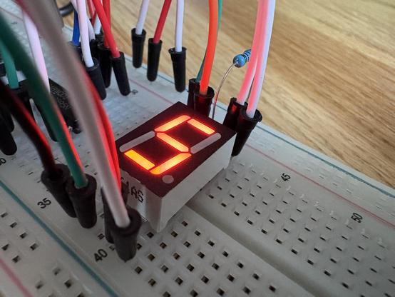 Eine Nahaufnahme eines Breadboards, auf das Kabel gesteckt sind und eine einzelne Ziffernanzeige, welche eine digitale "5" anzeigt.