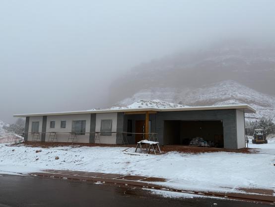 House being built with a bit of snow on the ground and the cliffs in the back shrouded by fog