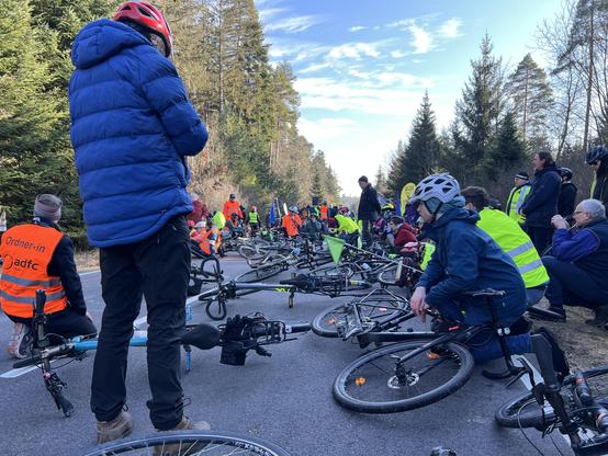 Alle TeilnehmerInnen haben als mahnende Geste im Gedenken an Natenom ihre Räder auf die Straße gelegt. Die Straße ist voll mit abgelegten Rädern. Dazwischen sitzen, knien oder Stehen deren BesitzerInnen