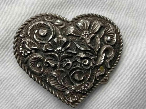 Heart-shaped belt buckle with detailed floral and decorative designs, outlined with a rope border.