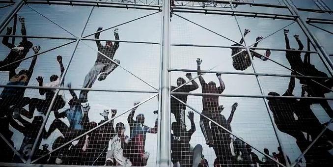 Screenshot aus dem Video "Borders" von Mathangi „Maya“ Arulpragasam, Künstlername M.I.A. - man sieht Menschen in einem Grenzzaun hängen.