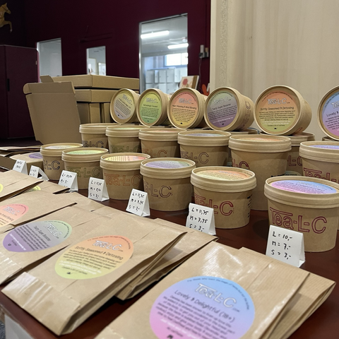 a little marketstall with beautiful small brown paperbags, medium and large brown paper cups. Colourful round labels on the frint of the bags and the lids of the cups describe what's in the lose leaf tea 
