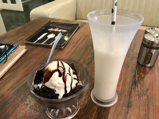 Das Foto zeigt ein großes Glas Kokosmilchshake und einen Brownie mit Eiscreme. 