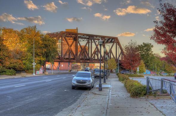 A street scene features a bridge in the background with cars parked along the road, framed by autumn foliage.