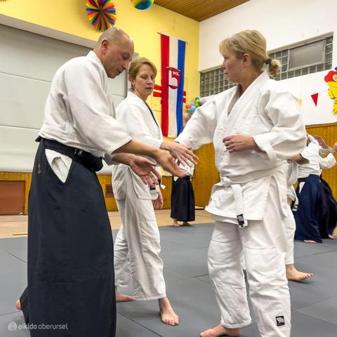 Male aikido teacher shows two female practitioners how to grab in an attack