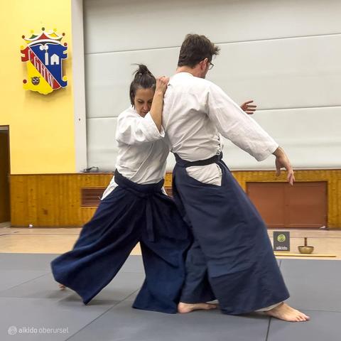 Female aikidoka shows a drop throw with a male attacker
