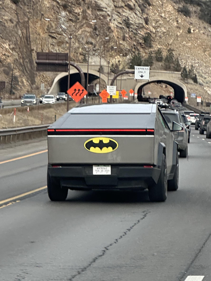 Picture of the rear end of a cybertruck out on the road with a Batman symbol on it like a child is driving it.  