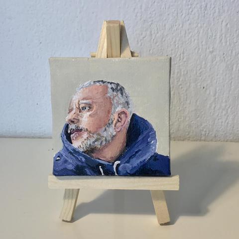 A small portrait painting on an easel of a person wearing a hoodie, looking off to the left