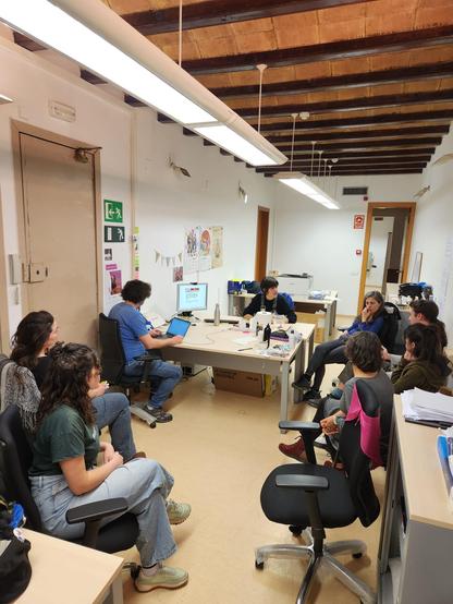 Gent de l'equip de NUS al voltant d'una taula prenent apunts i la Laura Vila Kremer explicant coses a l'altre cantó de la taula