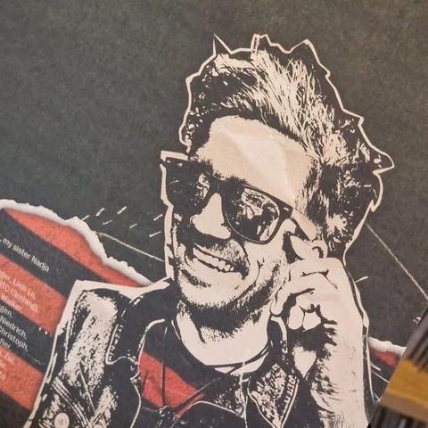 Eine stilisierte Schwarz-Weiß-Illustration eines lächelnden Mannes mit Sonnenbrille und stacheligen Haaren. Der Hintergrund verfügt über ein strukturiertes Design und farbenfrohe Akzente.
