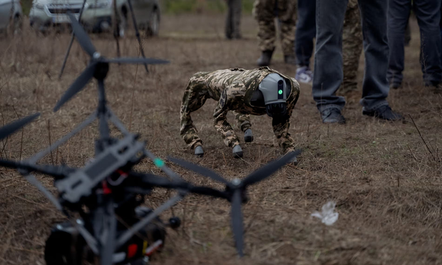 A robot dog and drone being tested for the Ukrainian military. The robot dog is wearing a brown camouflage suit and has a beady little green light on the front (which presumably turns red when it's set to 'kill')  

Photograph: Tetiana Dzhafarova/AFP/Getty Images