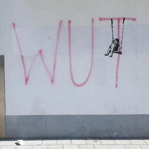 Grafitti des Hamburger Streetart-Künstlers NEAL an einer Hauswand: Am oberen waagrechten Strich des Buchstabens "T" des Wortes "WUT" hat NEAL das Grafitti eines schaukelnden und lachenden Mädchens platziert.