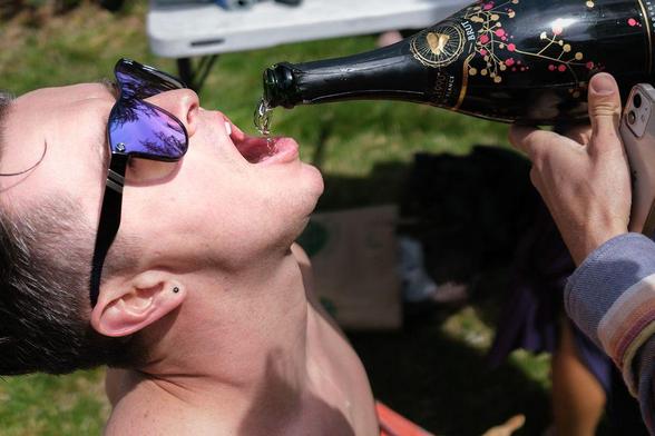 Shirtless man having champagne poured into his mouth.