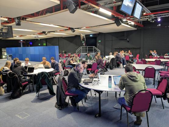 A couple of dozen developers sitting round tables in a big hall, pairing on Conway’s Game of Life.