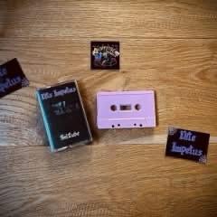 Eine Vintage-Kassette in einer Plastikhülle, eine violette Kassette und mehrere schwarze Aufkleber mit dem Text „Nite Impetus" auf einer Holzoberfläche.
