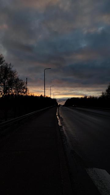 A road with a sunset and a car at the horizon