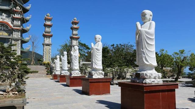 Row of white statues of standing disciples with hands in anjali.