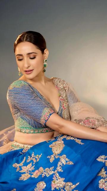 Pragya Jaiswal mesmerises in a blue lehenga by Dolly J, adorned with intricate embroidery and paired with a pale pink tulle dupatta. The structured cropped blouse adds a contemporary touch, while bold smokey eyes, red lips, and royal green jewellery elevate her fairy-tale-inspired ensemble.