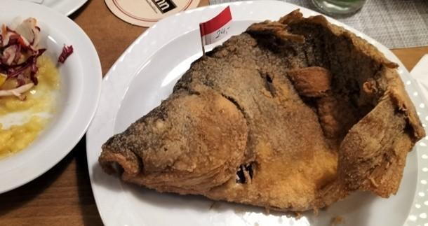 Gebackener Karpfen auf dem Teller mit rotem Fähnchen und der Aufschrift 24,- 
