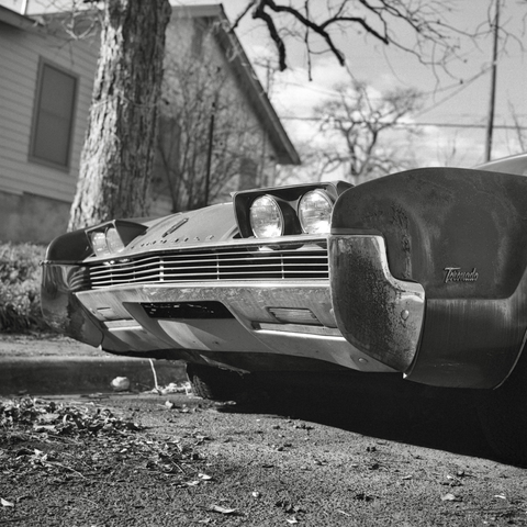 A black and white film photo. The weathered chrome on a vintage Oldsmobile Toronado shines in the sunlight in East Austin, Texas. Tuesday, February 4, 2025.