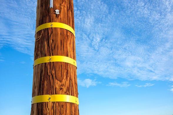 Power pole with bright yellow tape against partly cloudy blue sky.