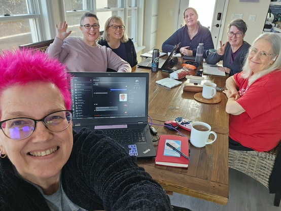 Six women sitting around a table, smiling because they’re happy to be conferencing together.