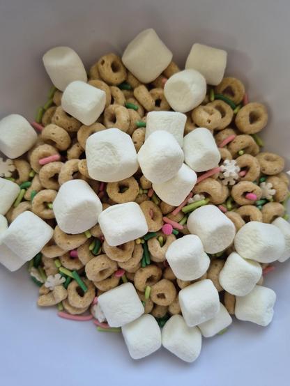 A close up photo of a bowl of cherrios mixed with marshmallows and pink and green sprinkles and little white snowflake sprinkles. So cute!