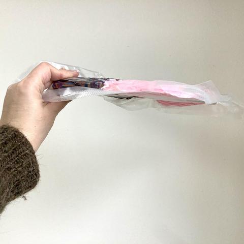 A hand holding up a very flat package containing yarn against a white background.