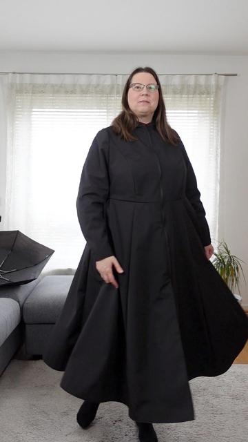 Full body image of a woman in a black raincoat. The full skirt is in motion.