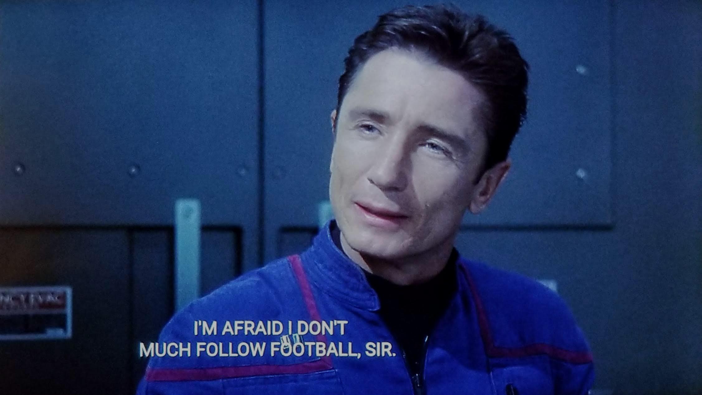 Star Trek Enterprise scene. We're on ship and looking at Malcolm Reed in uniform, sitting,  expounding, and probably eating pineapple held just off camera. Closed caption reads, "I'm afraid I don't much follow football, sir."