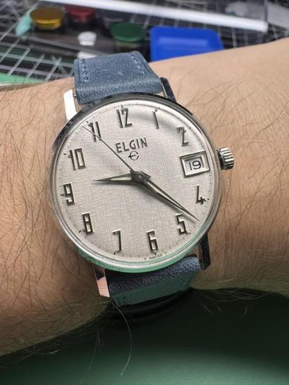 An Elgin mechanical watch with linen dial and silver arabic number indices on a blue strap
