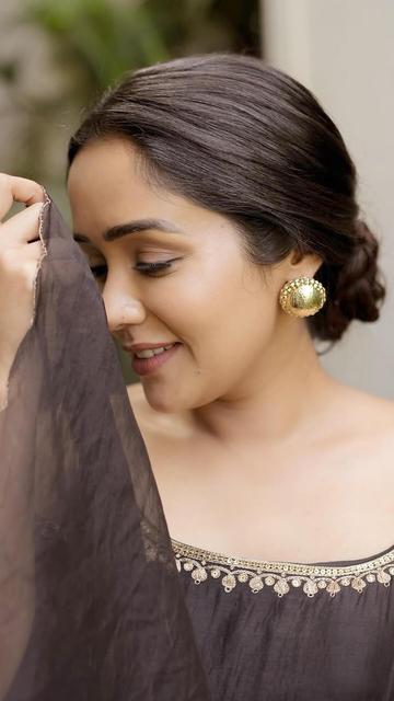 Ananya's recent black monochrome outfit showcases her impeccable fashion sense. The ensemble includes a sleeveless top with a wide neckline, adorned with intricate golden embroidery and sequins, flaring below the knee to create a graceful silhouette. She pairs this with matching black flared pants and a sheer dupatta featuring scalloped golden edges. Statement golden accessories, a sleek bun hairstyle, and elegant peep-toe sandals complete her chic look.