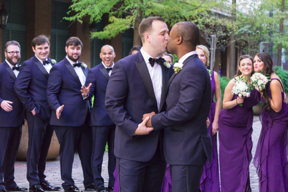 A wedding between two men, surrounded by the wedding party