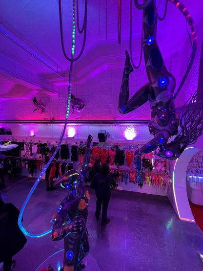Décor futuriste de Cyberdog : Une salle futuriste chez Cyberdog avec des sculptures lumineuses et des vêtements alternatifs. A futuristic room at Cyberdog with glowing sculptures and alternative clothing. Una sala futuristica da Cyberdog con sculture luminose e abiti alternativi.